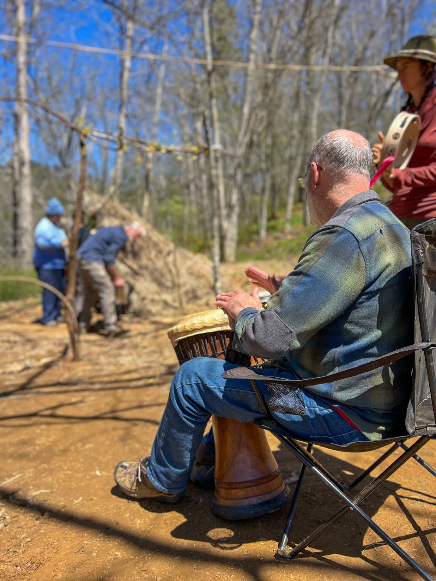 An elder playing a drum at a gathering in the woods